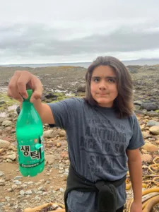 Boy holds up plastic bottle collected from the shoreline.